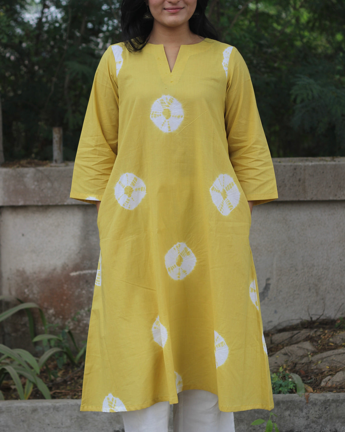 Yellow tie-dye cotton kurta with white bandhani print, V-neck, 3/4 sleeves, side pockets, and A-line design.