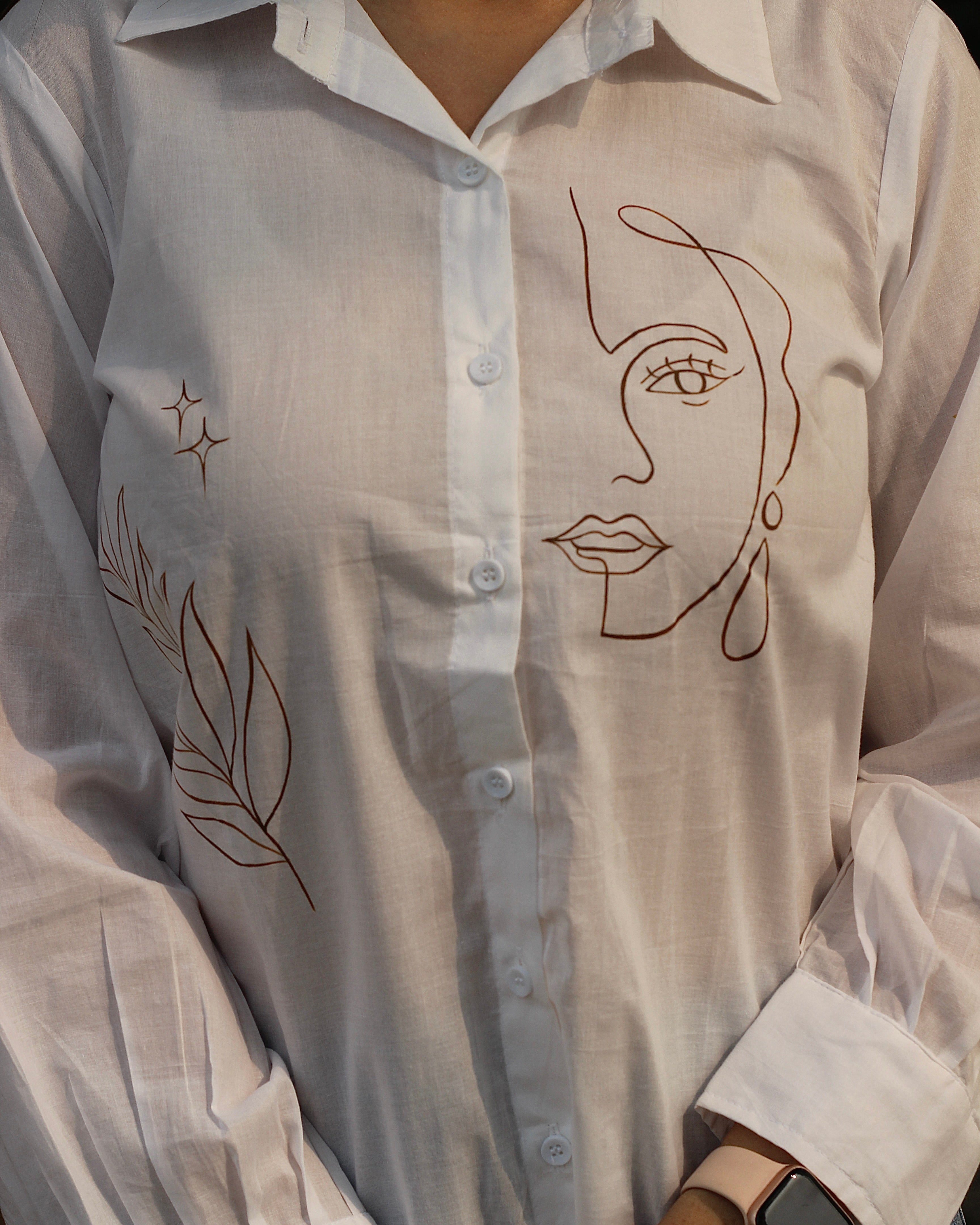 Hand-painted white shirt with bohemian brown leaf motifs, paired with jeans for a stylish look.